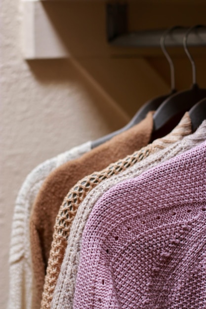 Nahaufnahme eines pastellfarbenen warmen Strickpullovers, der im Schrank hängt. Gemütliche Herbst- und Wintergarderobe