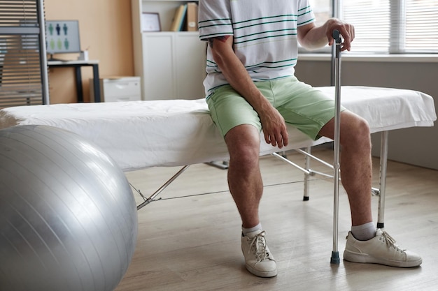 Nahaufnahme eines Patienten, der in einer Arztpraxis mit einer Krücke auf der Couch sitzt