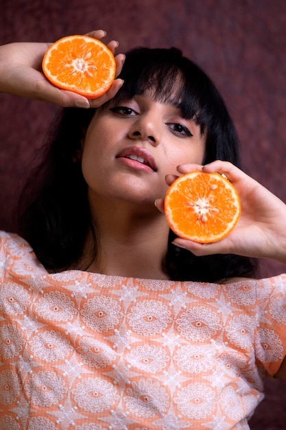 Nahaufnahme eines Portraits einer Frau, die eine Orange gegen die Wand hält