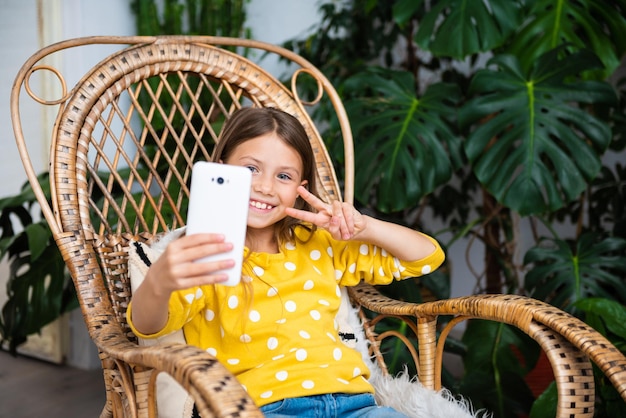 Foto nahaufnahme eines positiven kindermädchens, das remote-blogging mit dem smartphone studiert, beeindruckt von einem kommentar in einem sozialen netzwerk, der zu hause im schaukelstuhl sitzt