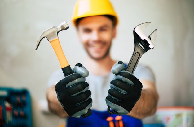 Nahaufnahme eines professionellen Mechanikers in Uniform und Schutzhelm hält in den Händen moderne neue Werkzeuge für Arbeit und Renovierung