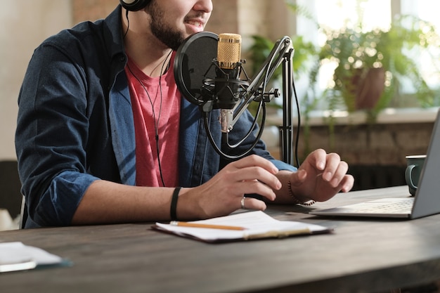 Nahaufnahme eines Radio-DJs, der am Tisch sitzt und im Mikrofon spricht, während er im Aufnahmestudio arbeitet