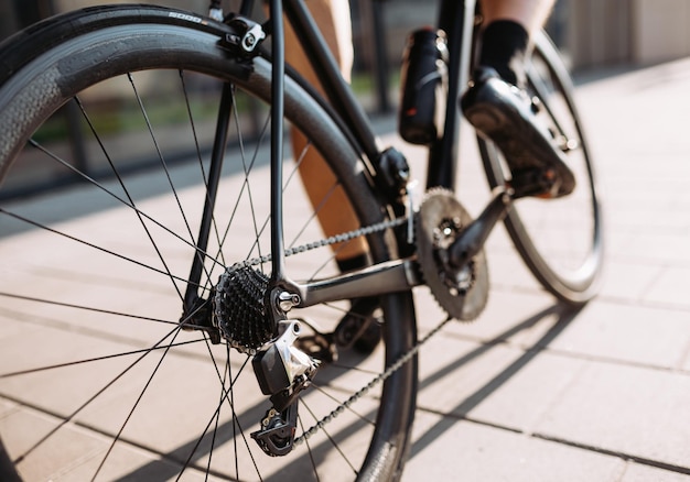 Nahaufnahme eines Radprofis mit muskulösen Beinen mit schwarzem Sportfahrrad für das Training im Freien Fokus auf Räder Regelmäßiges Training des Sportlers