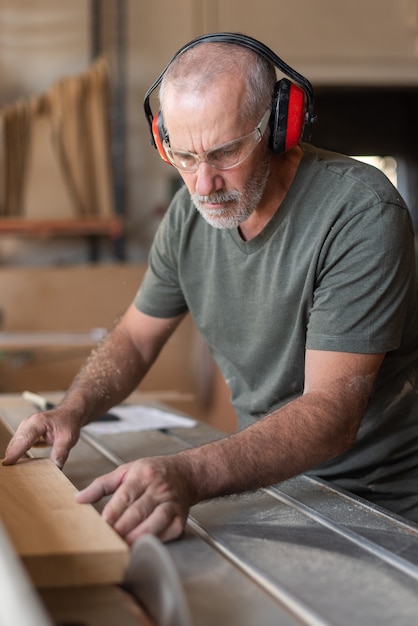 Nahaufnahme eines reifen Arbeiters, der in einer Fabrik ein Holz mit einer Maschine schneidet?