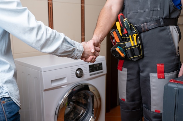 Nahaufnahme eines Reparaturmanns, der Händeschütteln mit einem weiblichen Kundenreparaturmann für Waschmaschinenreparatur schüttelt