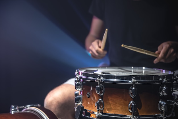 Nahaufnahme eines Schlagzeugers, der eine Snare-Drum mit Stöcken auf dunklem Hintergrund spielt.