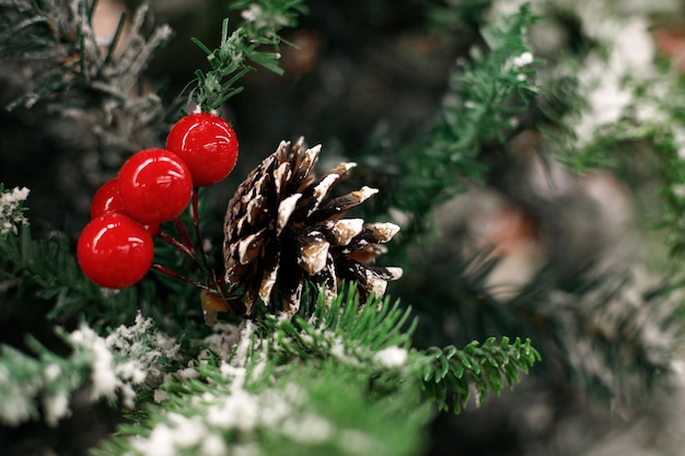 Nahaufnahme eines schneebedeckten Zweiges eines Weihnachtsbaums mit roten Beeren und einer Kiefernkugel