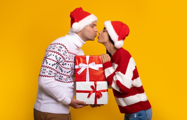 Foto nahaufnahme eines schönen glücklichen und aufgeregten jungen paares, das sich in weihnachtskleidung mit geschenkboxen in den händen verliebt, während sie neujahr feiern und sich gegenseitig beschenken