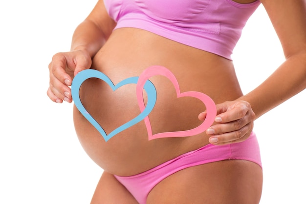Nahaufnahme eines schwangeren Bauches mit rosa und blauen Herzen Erraten Sie das Geschlecht des Babys oder der Zwillinge
