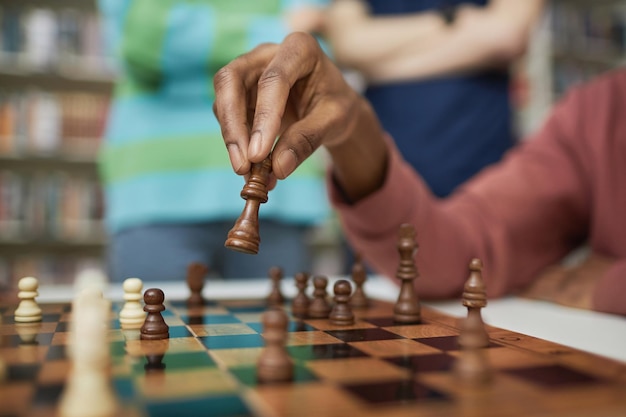 Nahaufnahme eines schwarzen jungen Mannes, der Schach spielt, während seine männliche Hand eine Schachfigur bewegt