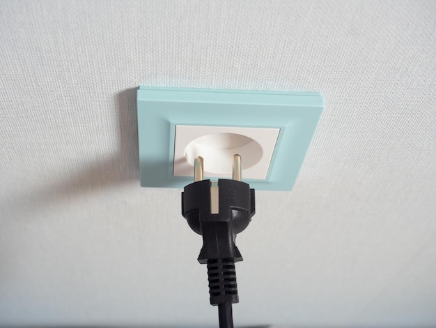 Nahaufnahme eines schwarzen Steckers in der Nähe einer blauen Steckdose an der Wand Das Konzept der Notwendigkeit von Elektrizität Elektrische Geräte, die für Kinder gefährlich sind
