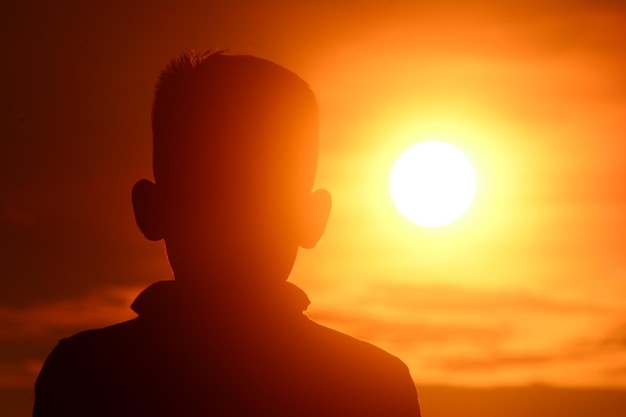 Foto nahaufnahme eines silhouettenjungen gegen den orangefarbenen himmel beim sonnenuntergang