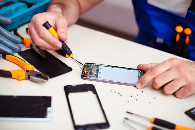 Nahaufnahme eines Spezialisten, während er ein defektes Smartphone an seinem Arbeitsplatz mit professionellen Werkzeugen repariert