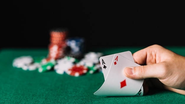 Nahaufnahme eines Spielers, der Karte mit zwei Assen auf Pokertabelle hält