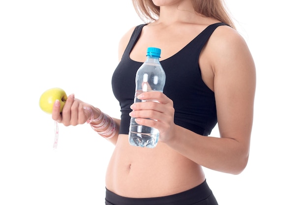 Nahaufnahme eines sportlichen Mädchens, das seitwärts gedreht ist und einen Apfel in der einen Hand und die andere eine Flasche Wasser hält