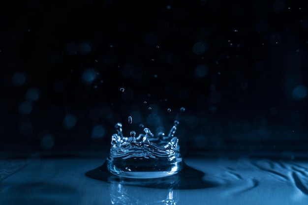 Nahaufnahme eines spritzenden Tropfens in blauem Wasser vor schwarzem Hintergrund