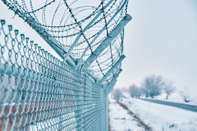 Nahaufnahme eines Stacheldrahtzauns an der Grenze im Winter, der für ein privates gesichertes Quarantäneobjekt in der Nähe von...