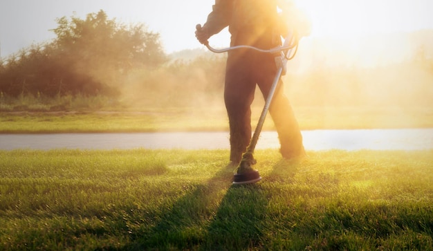 Nahaufnahme eines städtischen Arbeiters, der einen Rasenmäher in der Hand hält und das Gras in einem öffentlichen Park schneidet