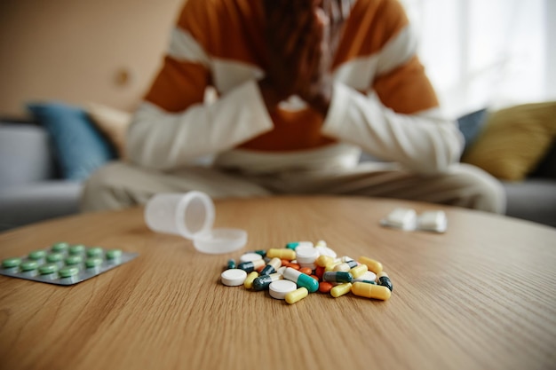 Foto nahaufnahme eines stapels pillen und tabletten auf dem tisch mit deprimiertem schwarzen mann im kopierraum im hintergrund