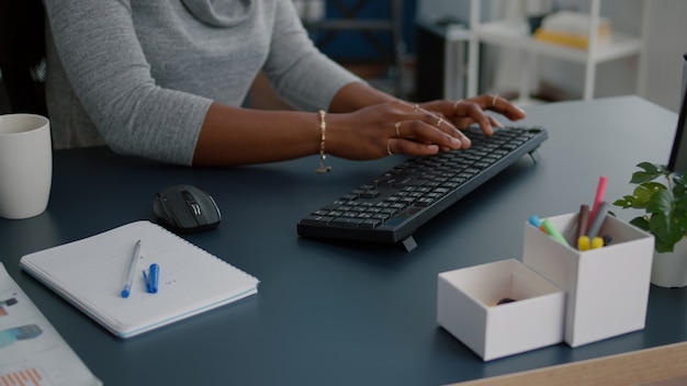 Nahaufnahme eines Studenten mit schwarzen Hauthänden, die auf der Tastatur nach Informationen suchen