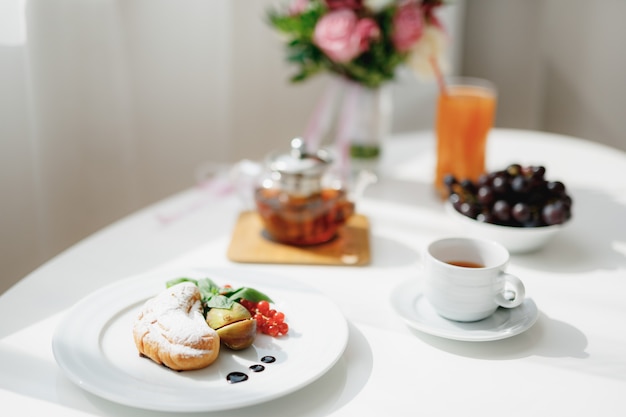 Nahaufnahme eines Tellers mit einem Croissant in Scheiben geschnittenen Feigen und einem Zweig roter Johannisbeeren auf einem weißen Tisch