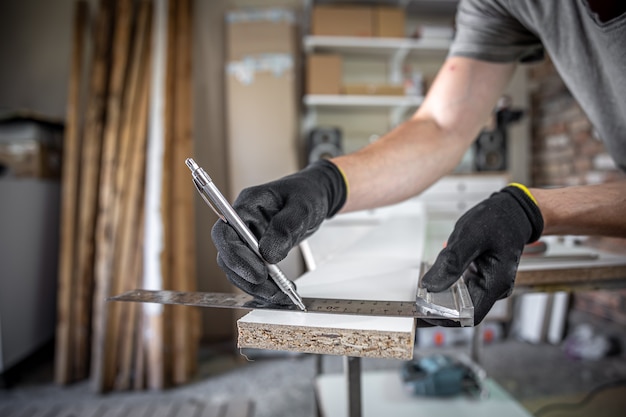 Nahaufnahme eines Tischlers, der Lineal und Bleistift hält, während er am Tisch in der Werkstatt Markierungen auf dem Holz macht.