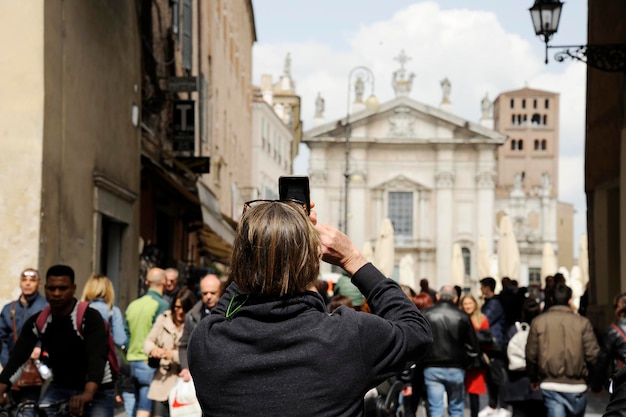 Nahaufnahme eines Touristen auf der Straße in Mantua, der mit dem Telefon ein Foto von der Piazza Sordello macht Mantua Italien