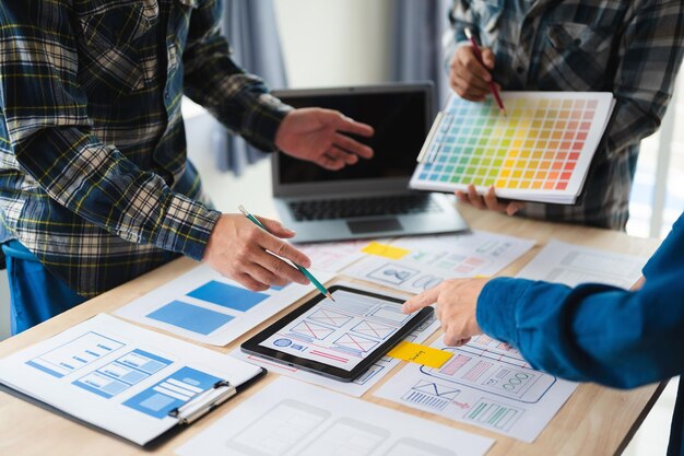 Nahaufnahme eines UI-Entwicklerteams, das mit einem Laptop, einem Smartphone und einem digitalen Tablet über sein Projekt brainstormt. Kreative digitale Entwicklungsagentur im Büro