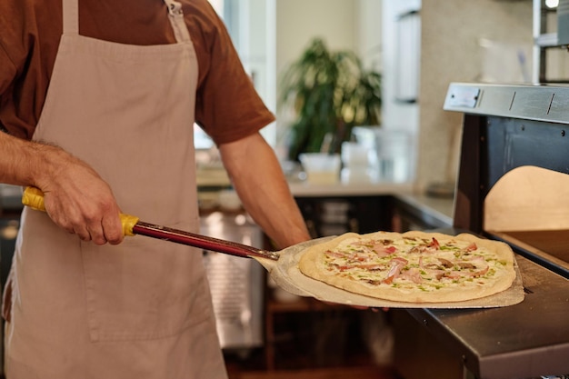 Nahaufnahme eines unbekannten kaukasischen Kochens, der mit einer Pizzaschale Pizza aus dem Ofen nimmt