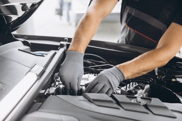 Nahaufnahme eines unerkennbaren Mannes mit grauem Handschuh, der den Motor und das Innere der Motorhaube des Autos inspiziert