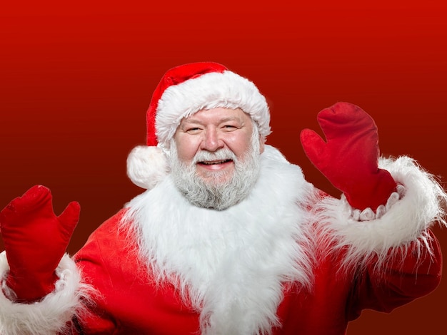 Nahaufnahme eines vorderen Bildes eines glücklichen Weihnachtsmannes, gekleidet in einen roten Mantel, mit Handschuhen und einem Hut, mit seinen erhobenen Händen hoch isolierten roten Hintergrund.