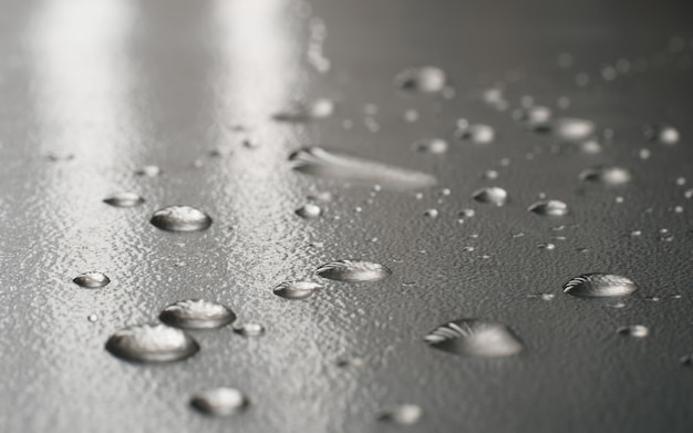 Nahaufnahme eines Wassertropfens auf einer grauen Oberfläche, niedriger Betrachtungswinkel, Perspektive. Makrofotografie von Wasser, nassem Hintergrund. Selektiver Fokus.