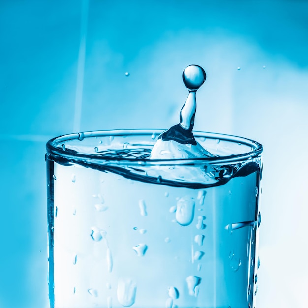 Nahaufnahme eines Wassertrops in einem Trinkglas vor blauem Hintergrund