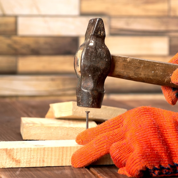 Nahaufnahme eines Zimmermanns in orangefarbenen Arbeitshandschuhen hämmert einen Nagel in ein Holzbrett