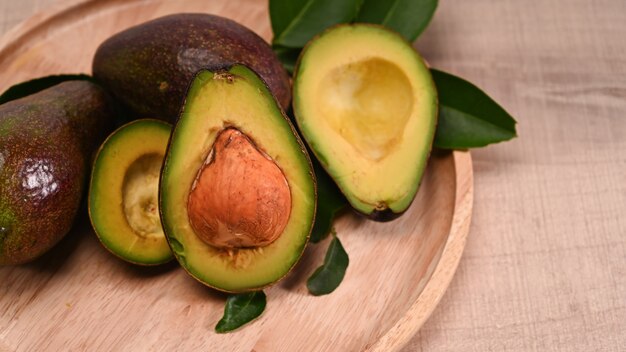 Nahaufnahme ganze Avocado und die Hälfte mit Samen auf Holzplatte.