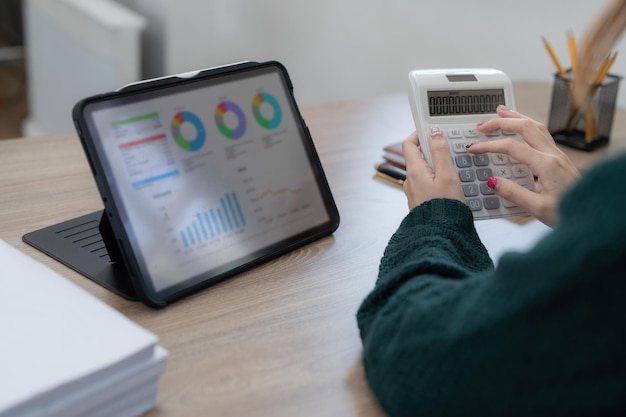 Nahaufnahme Geschäftsfrau, die Taschenrechner und Tablet für Mathefinanzierung auf Holzschreibtisch im Büro und Geschäftsarbeitshintergrund Steuerbuchhaltungsstatistik und analytisches Forschungskonzept verwendet