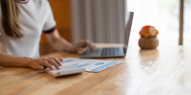 Nahaufnahme Geschäftsfrau mit Taschenrechner und Laptop für Mathefinanzierung auf Holzschreibtisch im Büro und im Geschäftsleben Hintergrund Steuerbilanzstatistik und analytisches Forschungskonzept