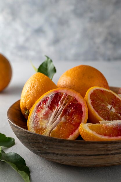 Nahaufnahme geschnittene blutige Orangen in Holzschale, auf hellem Hintergrund, ganz und Scheiben mit Blättern.