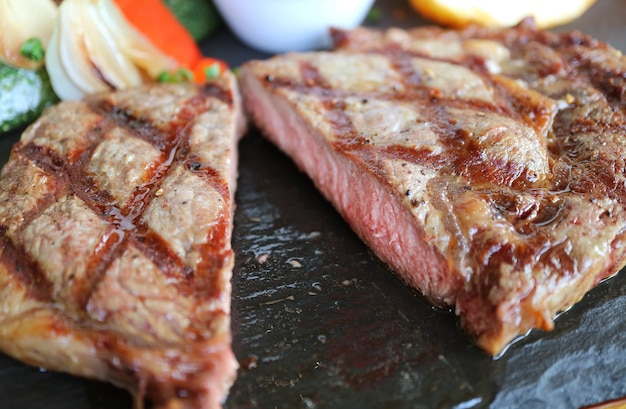 Nahaufnahme geschnittenes saftiges mittleres gegrilltes Ribeye-Steak, serviert auf einer heißen Steinplatte