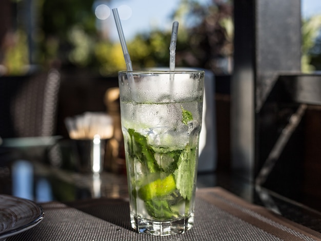 Nahaufnahme Glas des alkoholfreien Mojito-Cocktails mit Limette und Minze verziert mit Limettenscheibe und mit zwei Röhren am Barhintergrund.