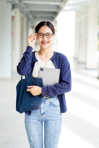 Nahaufnahme Glück fröhliche junge asiatische Studentin in lässiger Kleidung hält einen Laptop mit Touchbrille auf verschwommenem Schulgebäude Hintergrund Asiatisches Schulkonzept
