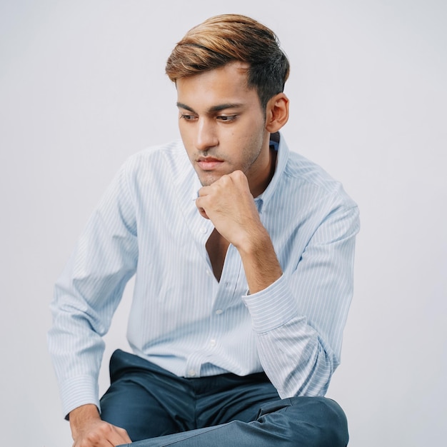 Nahaufnahme gut aussehender indischer junger Geschäftsmann denken sitzend Knopf isoliert graue Wand
