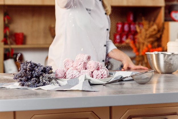 Nahaufnahme Hände des Küchenchefs bestreuen hausgemachte Marshmallows mit Zuckerpulver. Marshmallow-Vorbereitungsprozess. Das Konzept der Hausmannskost.