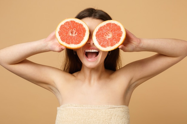 Nahaufnahme halbnackte Frau mit perfekter Haut nackt Make-up hält Grapefruit isoliert auf beige pastellfarbener Wand