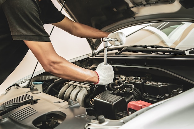 Nahaufnahme Hand des Automechanikers unter Verwendung des Schlüssels, um einen Automotor zu reparieren.