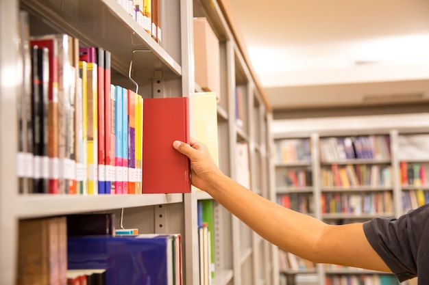 Nahaufnahme Hand, die ein Buch aus dem Bücherregal auswählt.