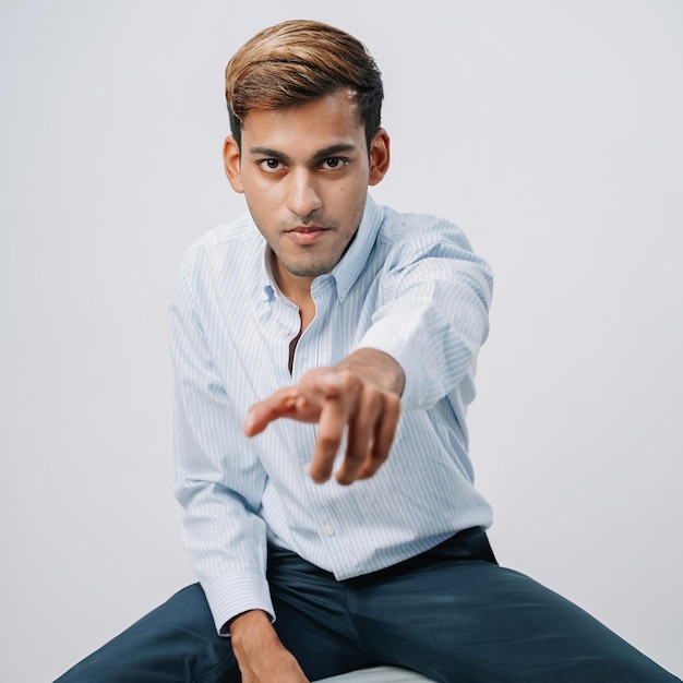 Nahaufnahme hübscher indischer junger Geschäftsmann, der auf eine ernste isolierte graue Wand zeigt