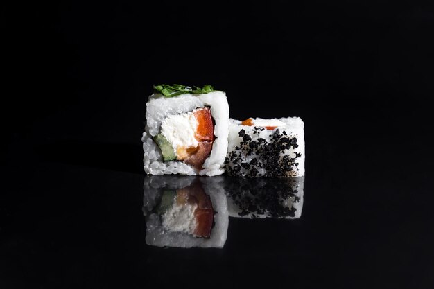 Nahaufnahme köstlicher Sushi-Rollen auf einem schwarzen, glänzenden Brett, horizontales Foto von Speisen auf schwarzem Hintergrund