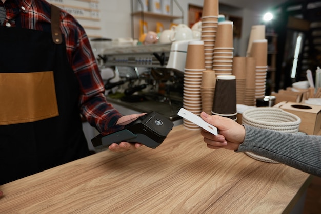 Nahaufnahme, Kundenhand, die Kreditkarte in der Nähe des NFC-Terminals hält. barista akzeptiert Zahlungen per Kreditkarte über den POS-Automaten im Café