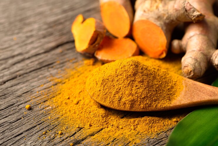 Nahaufnahme Kurkuma (Curcumin) Pulver im Holzlöffel mit frischem Rhizom auf Holzhintergrund.